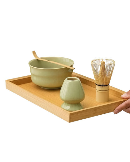 Tea-making set with green ceramic bowls, wooden spoon, and whisk on a wooden tray.