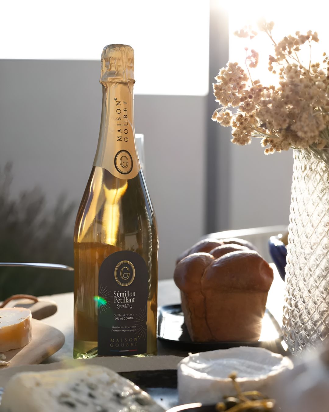 Maison Goubet sparkling non alcoholic drink bottle displayed on a table with cheese and bread in warm sunlight