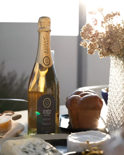Maison Goubet sparkling non alcoholic drink bottle displayed on a table with cheese and bread in warm sunlight