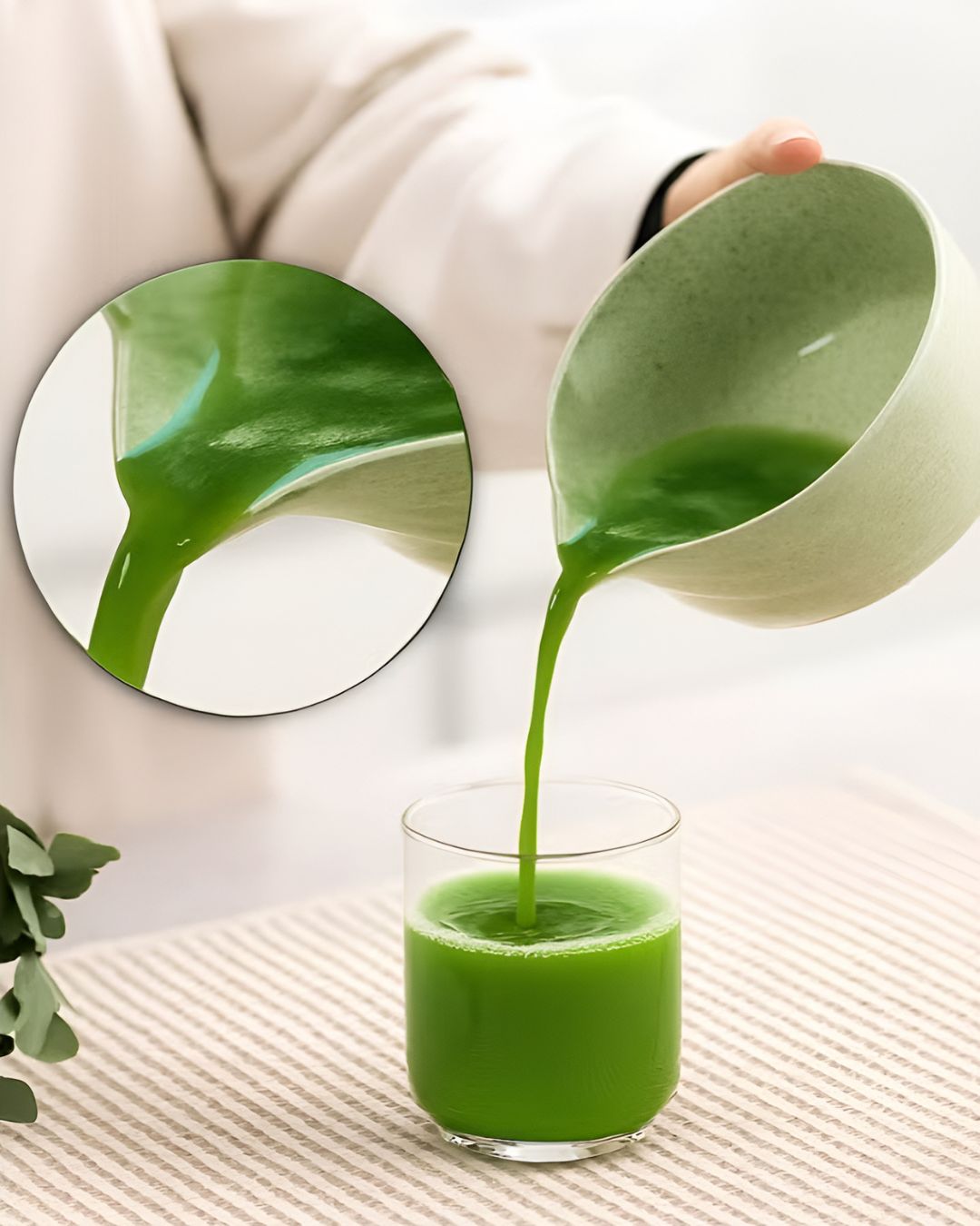 Green juice being poured from a pitcher into a glass with a close-up of a green leaf.