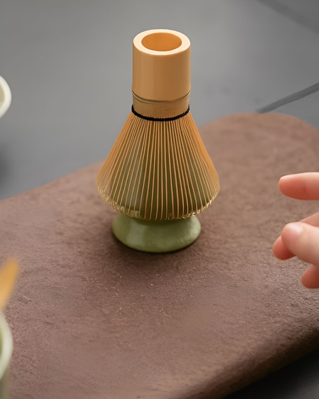 Bamboo whisk on a stone surface with a hand reaching towards it